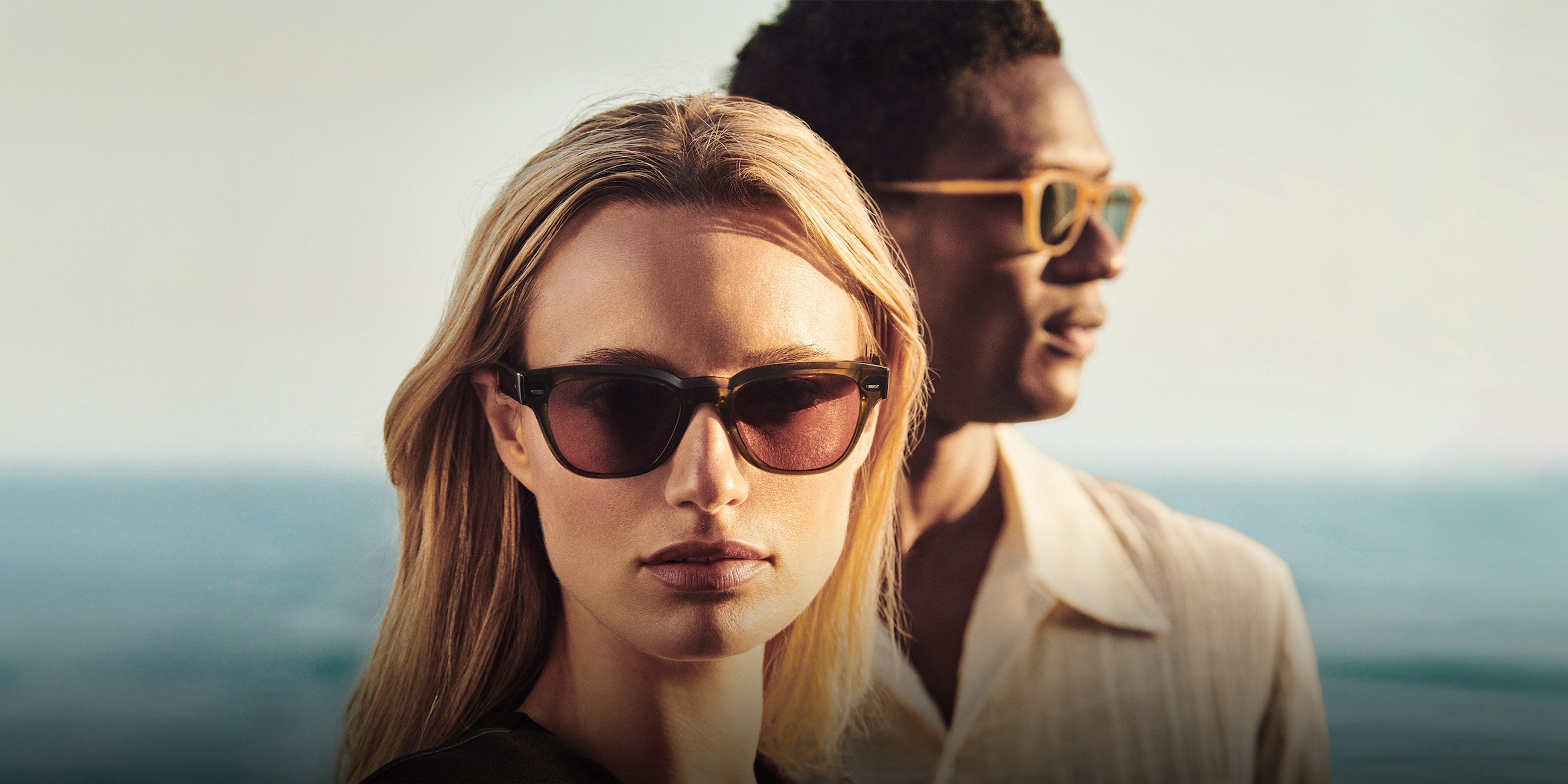 Rueny is seen in Hazel with Burgundy lenses alongside Emryn in Semi-Matte Goldwood with Blue lenses.